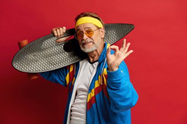 Kıdemli adam, Kırmızı Arkaplanda Yalıtılmış Pozisyon Verirken Uzun Tahtayla İyi Hareketler Gösteriyor ve Gülümsüyor 