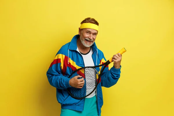 微笑的男人拿着网球火箭 在黄色工作室背景下 滑稽的资深网球选手在火箭上玩孤立游戏 游戏中的兴奋 人类情感 面部表情和对运动的激情 — 图库照片