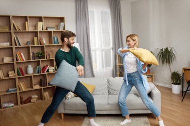 Evde Savaşan Yastıklar. Oturma odasında yastıklarla kavga eden mutlu genç çift. Pozitif Aile Birlikte Eğleniyor 