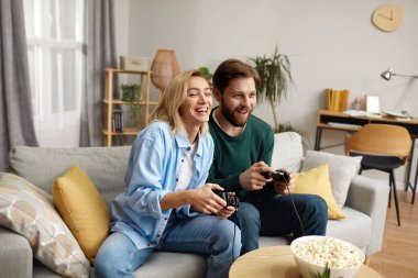 Video oyunları oynayan mutlu çift. Erkek arkadaşı ve kız arkadaşı oturma odasında oturup video oyunları oynayarak ve birlikte vakit geçirerek eğleniyorlar. Haftasonu Kavramının Keyifli Anı