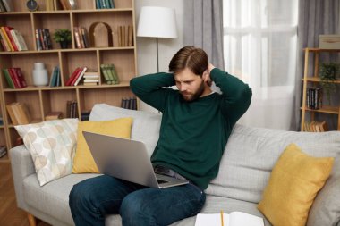 Bilgisayarda çalışan odaklanmış adam. Yakışıklı genç adam evde dizüstü bilgisayar kullanıyor. Öğrenci Erkekler Çalışma Odası. Çevrimiçi Alışveriş, Ev İşi, Serbest Çalışma, Çevrimiçi Öğrenme, Çalışma Konsepti