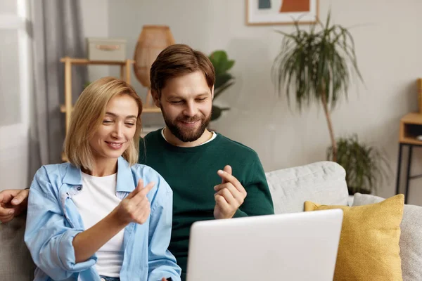 Couple Using Laptop Computer, While Sitting On The Living Room of Their Apartment. Boyfriend and Girlfriend Talk, Shop on Internet, Choose Product to Order Online, Watch Streaming Service