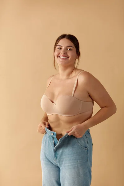 Plus Size Woman in Jeans. Overweight Smiling Woman Demonstrating Weight Loss. Happy Girl Showing Large Jeans And Looking At Camera