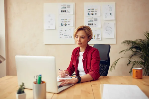 Calm Business Woman Working At Office. Focused Lady Using Laptop Writing Notes. Female Person Sitting At Workplace In Modern Office. Successful Entrepreneurship And Career Concept