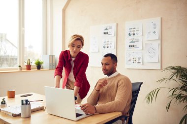 Smiling Colleagues Working Laptop At Office. Happy Business Couple Using Computer In Modern Office. Woman Giving Advices To Man. Teamwork Concept