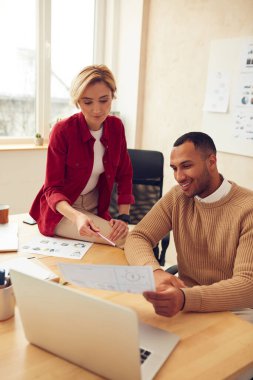Smiling Colleagues Working At Office. Happy Business Couple Discussing Documents Using Computer In Modern Office. Woman Giving Advices To Man. Teamwork Concept