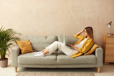 Woman Using Laptop At Sofa. Young Girl Holding Computer, Sitting At Home On Cozy Couch. Caucasian Lady Relaxing With Laptop Alone 