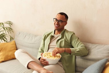 Smiling Man Watching TV. Multiracial Guy Eating Popcorn While Watching Movie Alone, Resting At Couch, Spending Weekend At Home