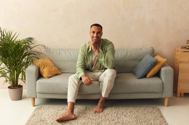 Happy Man Relaxing Sofa. Smiling Middle Eastern Guy Sitting On Comfortable Couch And Posing At Home In Living Room. Cheerful Man Relaxing On Sofa, Enjoying Weekend