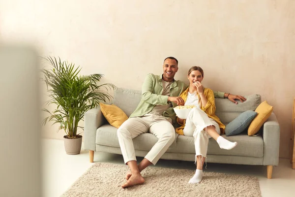 Happy Couple Watching TV At Home. Loving People Resting On Sofa And Eating Popcorn At Cozy Home Morning. Leisure Concept 