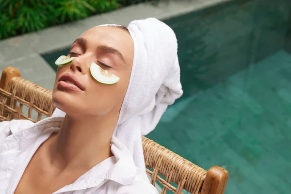 Relaxed Woman With Cucumber Mask. Young Bathrobe Girl Relaxing With Cucumber Slices Under Eyes Near Swimming Pool. Concept of Skincare