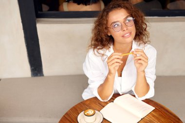 Online Work At Cafe. Thoughtful Woman Girl In Glasses Holding Pen While Working In Restaurants. Remote Job Or Education With Modern Digital Technologies For Comfortable Lifestyle In City