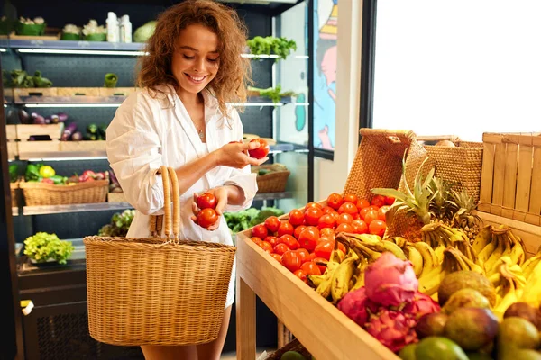 Organic Food. Smiling Woman Holding Basket And Choosing Fresh Vegetables While Buying Goods At Bio Grocery Store. Shopping And Customer Concept