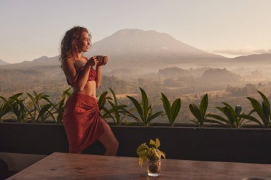 Kadınlar yoga inzivasında kahvenin tadını çıkarıyorlar lüks bir tatil köyünde Agung volkanı ve Bali 'deki güzel gündoğumunun muhteşem manzarasıyla..