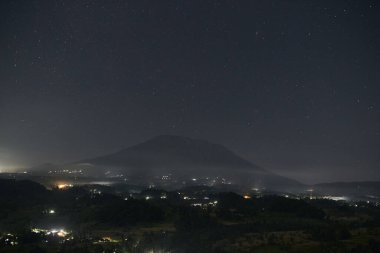 Gece volkanı Agung. Gece Işıklarındaki Tropik Volkanik Dağlar. Krater ile aktif volkan. Karanlık Gökyüzü ile Akşam Manzarası