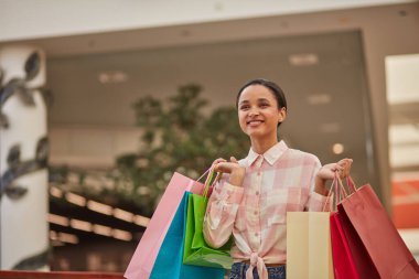 Mağazada alışveriş torbaları taşıyan, gülümseyen ve alışveriş yapmaktan zevk alan bir kadın..