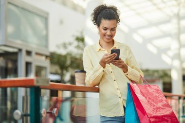 Şehirde alışveriş torbasıyla alışveriş yaparken telefonunu kullanan bir kadın. Mutlu ve modaya uygun görünüyor, dışarıda eğleniyor..