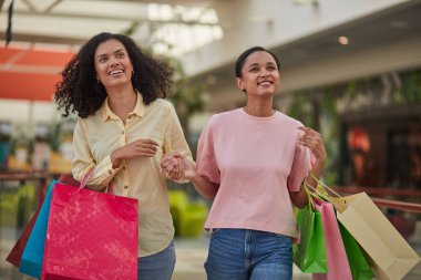 Arkadaşları olan mutlu bir kadın alış veriş merkezinden zevk alıyor, gülümsüyor ve alışveriş torbalarıyla alışveriş merkezinde koşuyor..