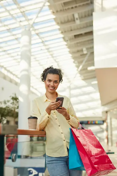 Seorang Wanita Memegang Tas Belanja Dan Tersenyum Saat Menggunakan Ponsel — Stok Foto