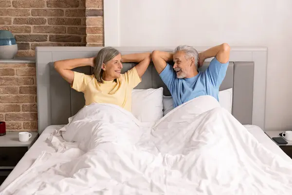 Two people relaxing in a bedroom together, lying.on a bed.