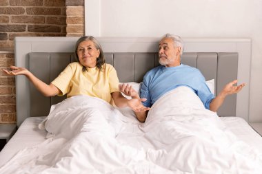 Yatakta oturan yaşlı bir çift ellerini yan yana omuz silkiyor..