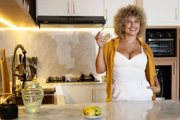 Smiling Curly Haired Woman Holding Glass Water While Standing Stylish — Stock Photo, Image