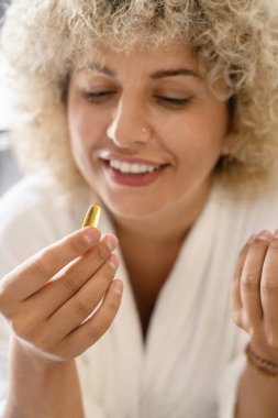 Sağlıklı beslenme. Omega-3 kapsülü tutan mutlu genç kadın, günlük sağlık desteği. Genç bayan elinde altın bir Omega-3 kapsüle bakıyor. Sağlıklı Yaşam Tarzı ve Besleyici İlaveler.