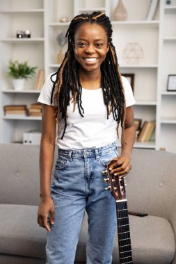 Neşeli genç Afrikalı Amerikalı kadın elinde gitarıyla hobilerinin keyfini çıkarmaya hazır. Samimi bir iç mekanda gündelik hayatın rahatlığını ve mutluluğunu yayıyor..