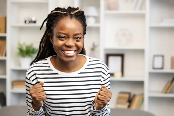 ハッピーアフリカ系アメリカ人女性の笑顔は 彼女の居心地の良い よく組織されたホームオフィススペースに座って 自信と成功を感じながら 達成を祝います — ストック写真