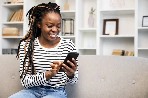 Eine Afroamerikanerin Mit Dreadlocks Lächelt Mit Einem Smartphone Hause Und — Stockfoto