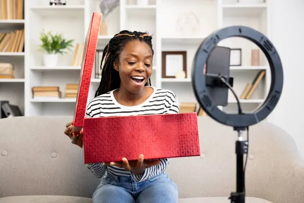 Nadšený Mladý Afroameričanka Doma Radostně Rozbaluje Červený Balíček Překvapením Potěšením — Stock fotografie