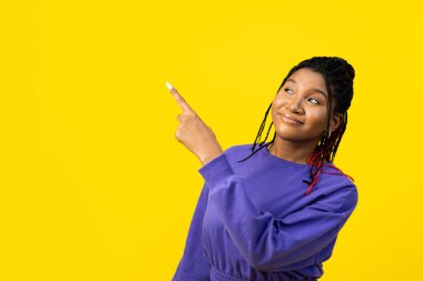 Yanları gösteren genç bir kadın, parlak sarı bir arka planda izole edilmiş bir şekilde, pozitif ve coşkulu bir şekilde yüzünü çeviriyor..