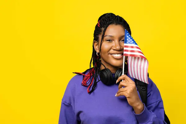 Stock image Woman holding a small american flag and wearing headphones on yellow background