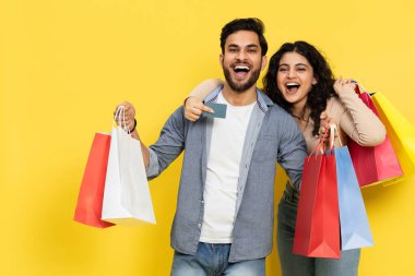 Renkli alışveriş torbaları ve sarı arka planda kredi kartı olan neşeli çift heyecanlı alışveriş seti, mutlu satışlar.