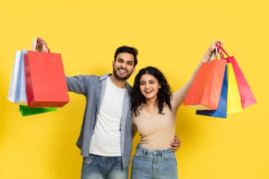 Mutlu çift alışverişi Parlak sarı arka planda birden fazla renkli çantaları olan alışveriş terapisinin tadını çıkarıyor.
