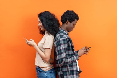 Bağlı Ama Tek Başına: Canlı Turuncu Arkaplan, Sosyal Medya, İletişim ve Modern Yaşam Tarzı Konsepti Üzerine Akıllı Telefonlara Kapılmış İki Genç Yetişkin.