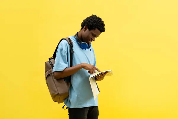 黄色い背景のアドベンチャーマップを探索する若い学生 そして発見の概念 カジュアルバックパックとブルーシャツを着て トリッププランニングに従事 季節的な探査 — ストック写真