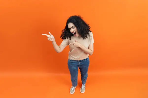 Aufgeregte Junge Frau Zeigt Überrascht Auf Orangefarbenen Hintergrund lizenzfreie Stockbilder