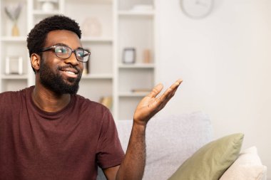 Evdeki koltukta el hareketleriyle oturan mutlu Afrikalı Amerikalı adam. Rahat, güler yüzlü, rahatlatıcı yaşam tarzı konsepti. Konforlu Modern Oturma Odası İçi.