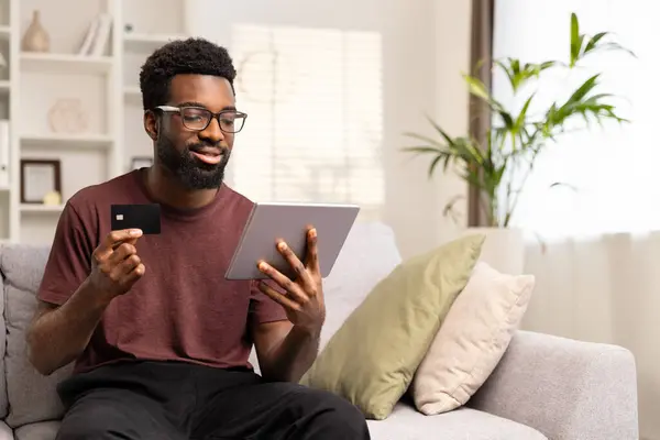 笑顔のアフリカ系アメリカ人男性は クレジットカードとタブレットでオンラインショッピングをします Eコマースとオンライン決済コンセプト 選択的なフォーカス コピースペース ロイヤリティフリーのストック画像