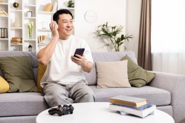 Evde kulaklıkla müzik dinleyen mutlu bir adam, akıllı telefon, gündelik ve boş zaman kavramı kullanarak gülümsüyor..