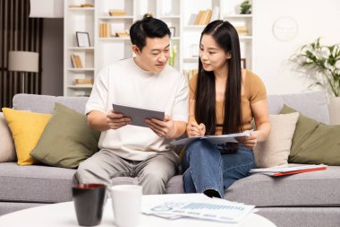 Evde tablet ve belgelerle bir proje üzerinde işbirliği yapan iki kişi, takım çalışmasını ve üretkenliği gündelik bir ortamda gösteriyor