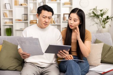 Finansal belgeleri analiz eden ve koltukta dijital tablet, ev finansmanı ve bütçe planlama kavramını inceleyen çift.