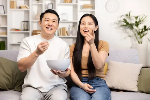 Joyful Asian Couple Sharing Light Moment While Eating Snacks Living — Stock Photo, Image
