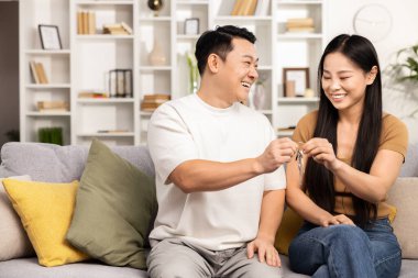 Kanepede anahtarlarını değiş tokuş eden mutlu bir çift, yeni ev kavramı, taşınma, birliktelik ve güzel dekore edilmiş modern bir oturma odasında neşeli bir ev sahibi.