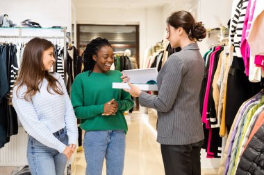 İyi, çeşitli kadınların moda alışverişini, perakende satış deneyimini sevdiği bir kutunun asistanıyla kıyafet mağazasında alışveriş yapan mutlu müşteriler.