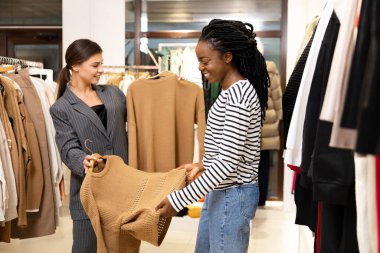 Danışmanla Alışveriş yapan Kadın, Butikte Kazak Deniyor. Görüntü Moda ile Neşeli Bir Etkileşim Yakalıyor, Perakende ve Yaşam Tarzı Konseptlerini Desteklemek İçin İdeal.
