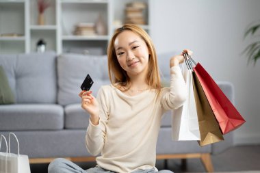Alışveriş poşetleriyle evde kredi kartı gösteren mutlu kadın. Perakende satış terapisi, çevrimiçi alışveriş ve tüketim için ideal..