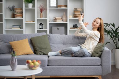 Rahat bir oturma odasında, rahat bir yaşam tarzında ev içi rahatlığı, modern ev içi iç mekanda selfie çeken genç bir kadın.