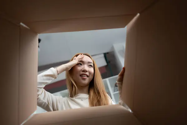 Surprised Asian Woman Looking Cardboard Box Expressing Excitement Curiosity Unboxing ภาพสต็อก